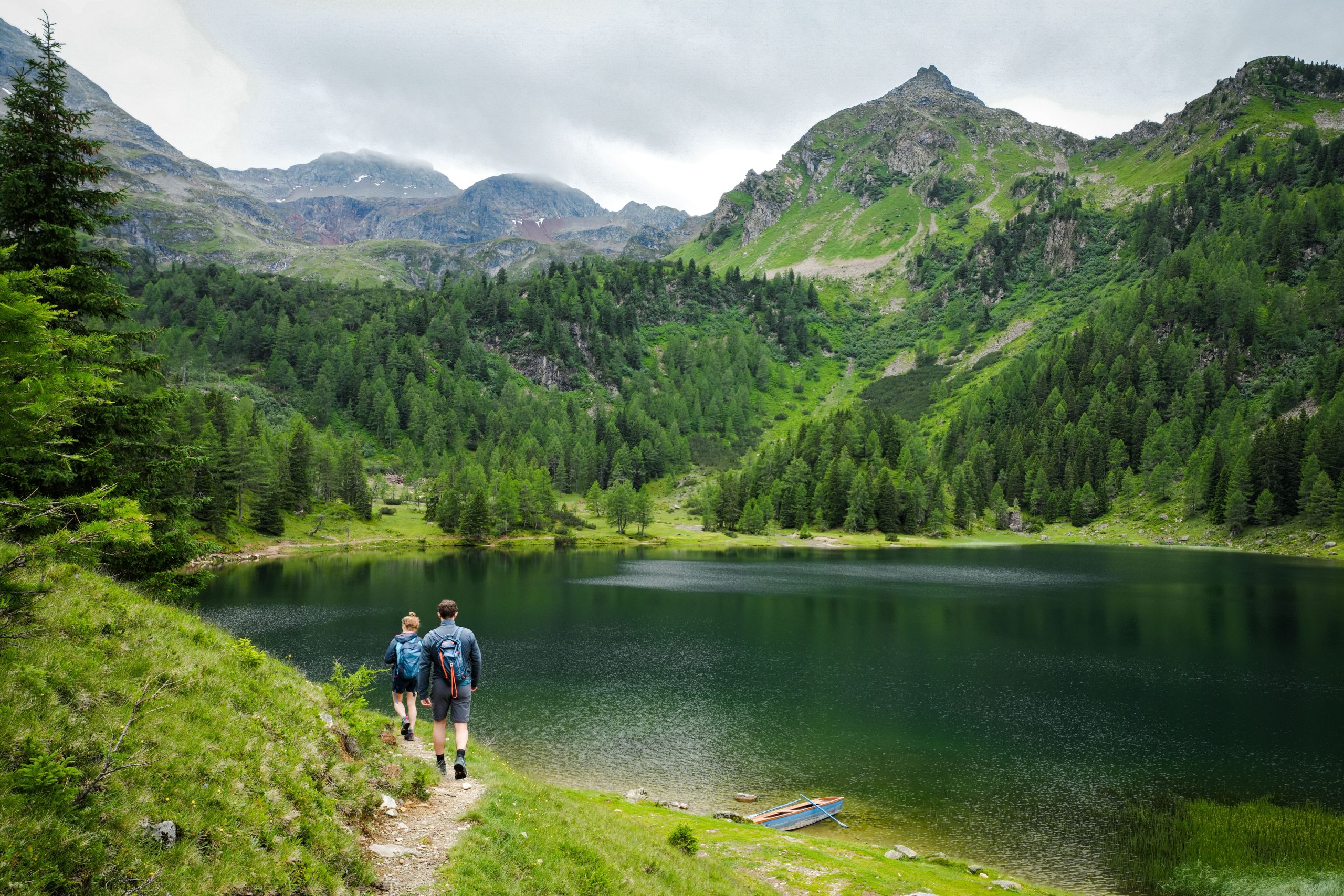 Randonneurs sur sentier alpin avec lac montagneux verdoyant