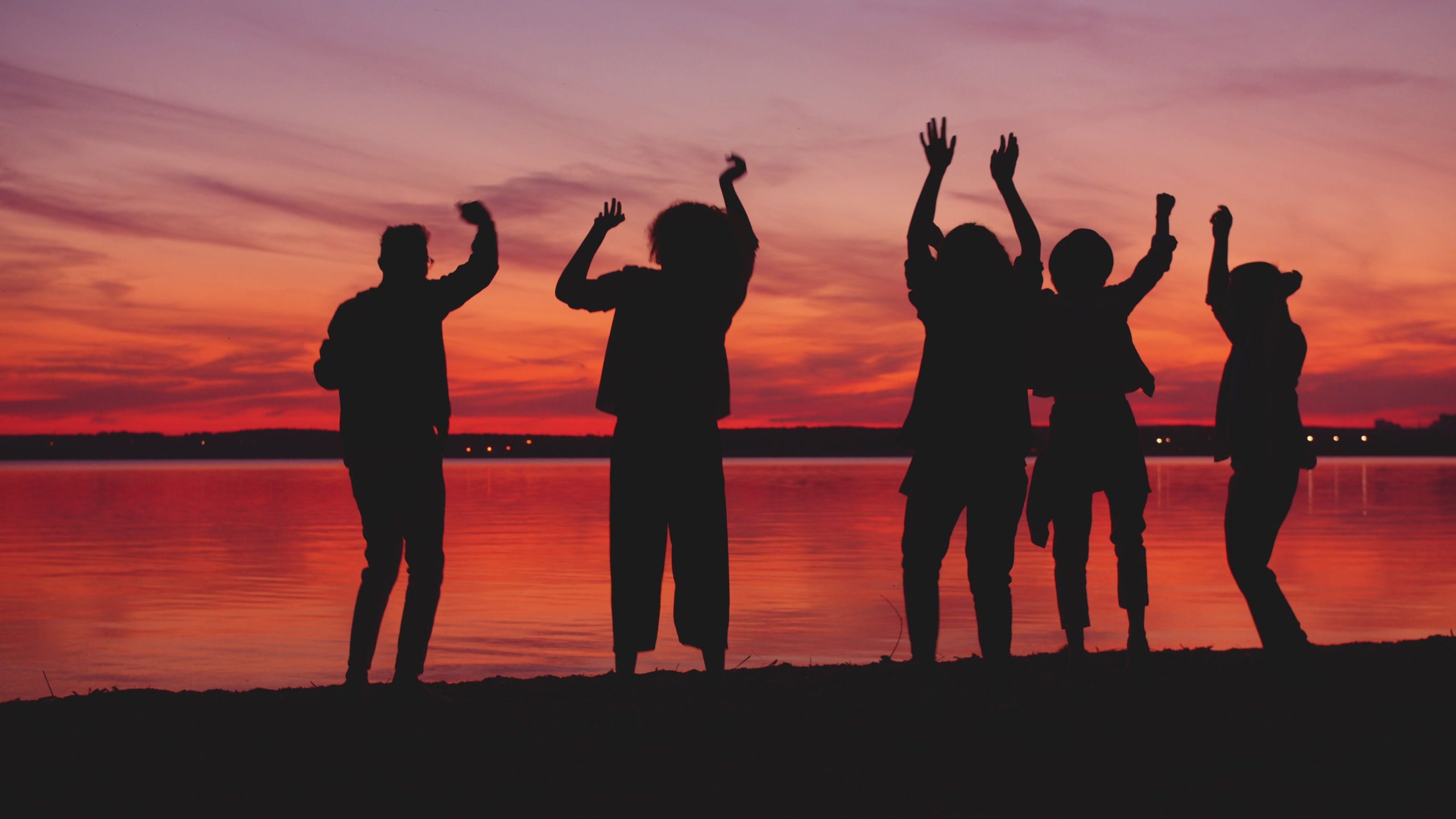 Groupe de personnes dansant près d'un lac au coucher soleil